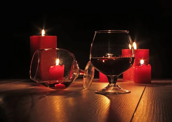 Glass of cognac and red candle on a wooden background — Stock Photo, Image