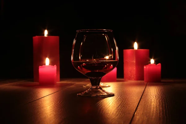 Vidro de conhaque e vela vermelha em um fundo de madeira — Fotografia de Stock