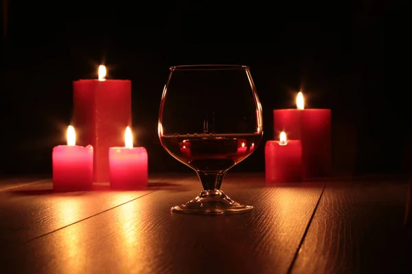 Glass of cognac and red candle on a wooden background — Stock Photo, Image
