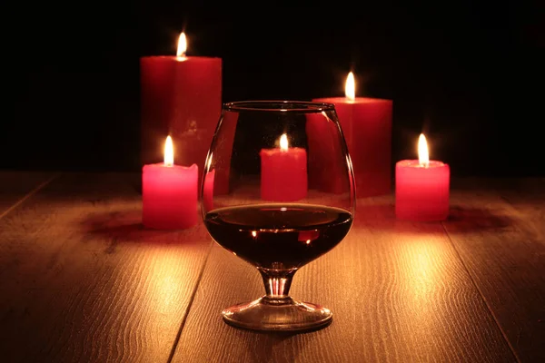 Glas Cognac und rote Kerze auf Holzgrund — Stockfoto