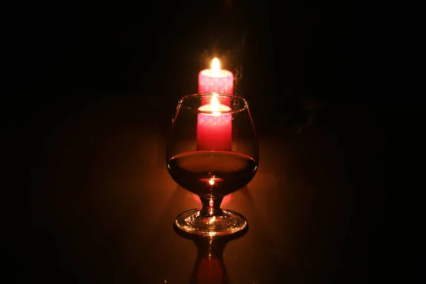 Copo de conhaque ou conhaque e vela na mesa de madeira — Fotografia de Stock