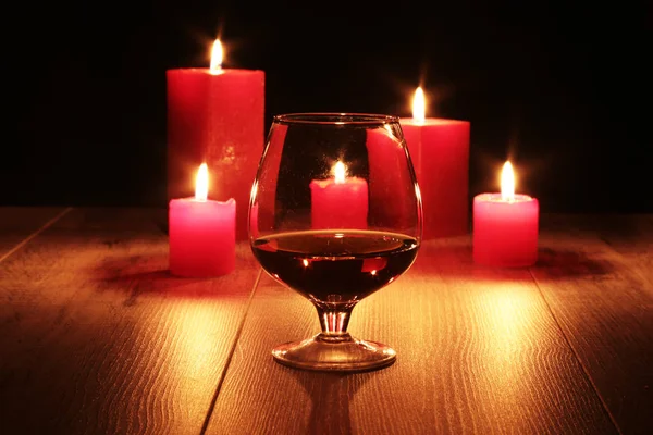 Glass of cognac and red candle on a wooden background. — Stock Photo, Image