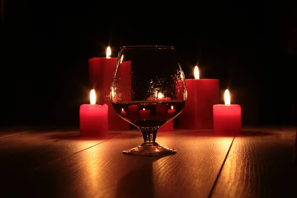 Glass of cognac and red candle on a wooden background. — Stock Photo, Image