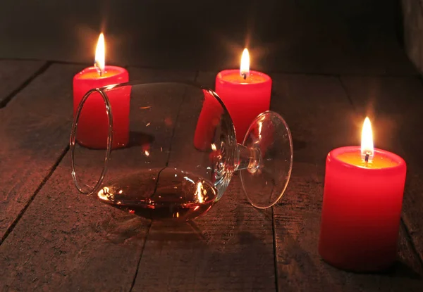 Glass of wine or cognac and red candle on a wooden background. — Stock Photo, Image