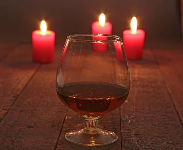 Glas wijn of cognac en Rode kaars op een houten achtergrond. — Stockfoto