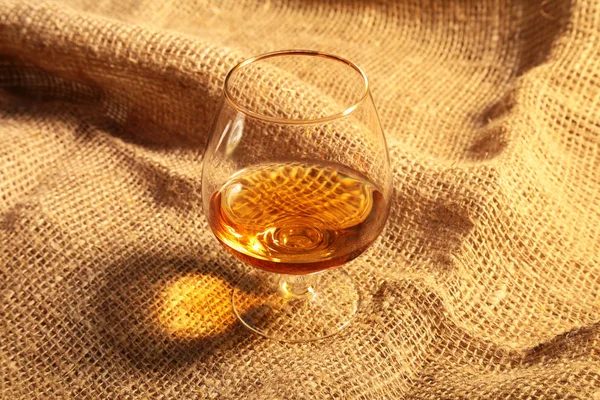 Cognac i ett glas, praliner på gammal textil säckväv — Stockfoto