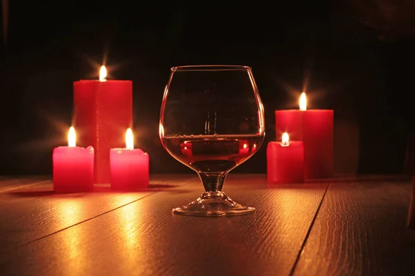 Vaso de brandy o coñac y vela sobre la mesa de madera —  Fotos de Stock