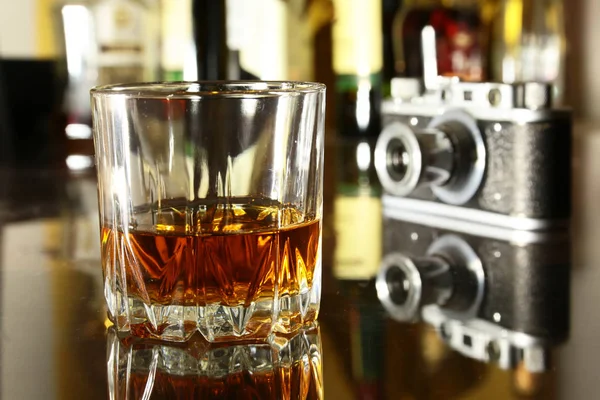 Glas av brandy eller cognac och retro kamera på tabellen spegel trä — Stockfoto