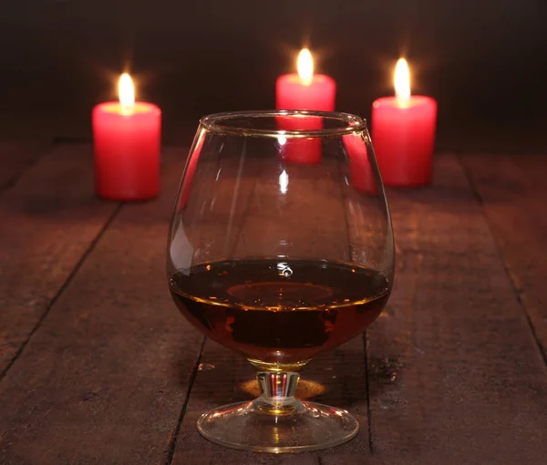 Glas wijn of cognac en Rode kaars op een houten achtergrond. — Stockfoto