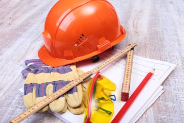 Turuncu kask, koruyucu gözlük, eldiven ve ahşap arka plan üzerinde ölçüm bandı.