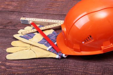 Turuncu kask, koruyucu gözlük, eldiven ve ahşap arka plan üzerinde ölçüm bandı.