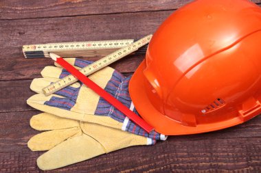 Turuncu kask, koruyucu gözlük, eldiven ve ahşap arka plan üzerinde ölçüm bandı.