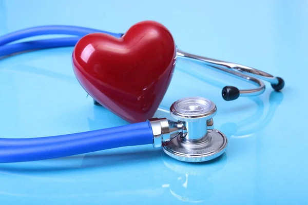 Estetoscópio médico e coração vermelho isolado no fundo do espelho azul . — Fotografia de Stock