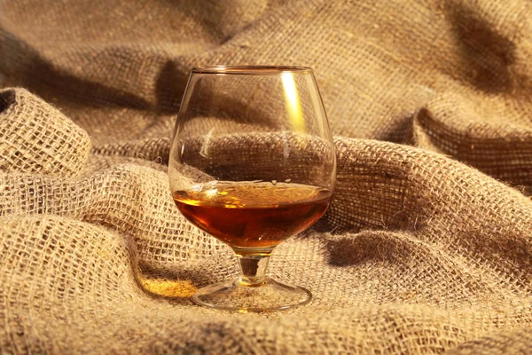 Cognac i ett glas, praliner på gammal textil säckväv — Stockfoto