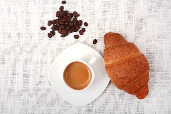 Хрусткі свіжі круасани та чашка кави еспресо на білому тлі, ранковий сніданок, вибірковий фокус — стокове фото