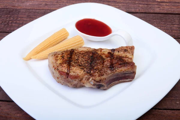 Chuleta de cerdo a la parrilla con salsa de arándano y mini mazorca de maíz conservada en placa sobre tabla de madera — Foto de Stock