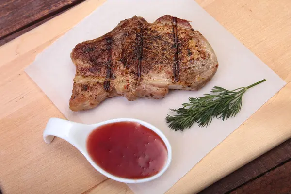 Chuleta de cerdo a la parrilla con salsa de arándano en plato sobre tabla de madera — Foto de Stock