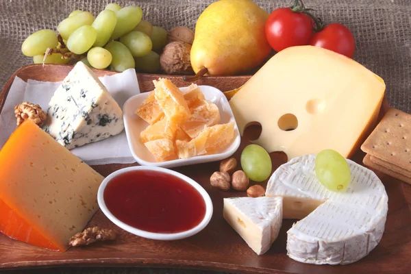 Ассортимент сыра с фруктами, виноградом и орехами на деревянном подносе . — стоковое фото