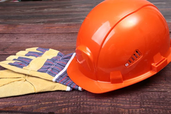 Orange hard hat and gloves for work on wood background.