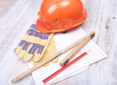 Turuncu kask, koruyucu gözlük, eldiven ve ahşap arka plan üzerinde ölçüm bandı.