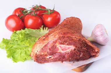 Çiğ domuz knuckle ve sebze, sarımsak, domates baharat ve marul yaprakları bir kesme tahtası üzerinde. Seçici odak. Hazır yemek pişirmek için.