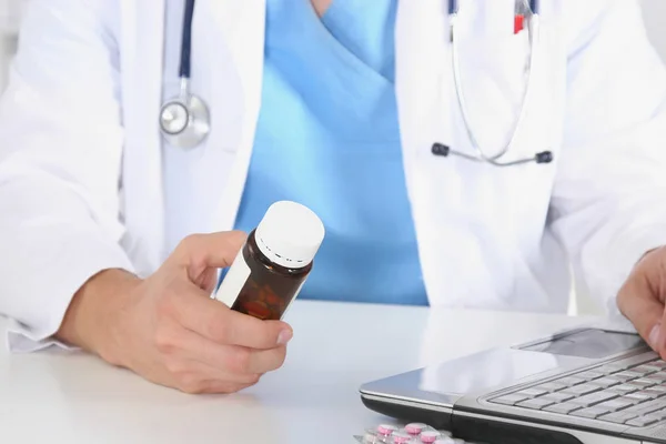 Lekarz mężczyzna siedział przy stole, trzymając w ręku wiele różnych tabletek. — Zdjęcie stockowe