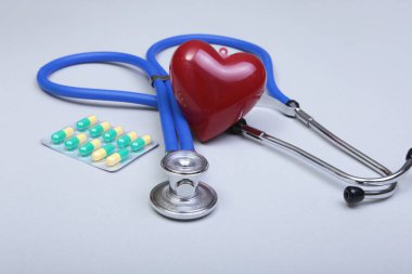 Beyaz arka plan üzerinde RX reçeteli, stetoskop, pils ve kırmızı kalp.