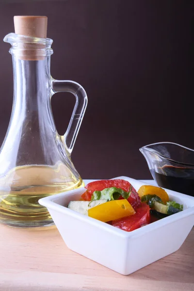 Salada de legumes frescos com tomate, pepino, pimentão, folha de alface em tigela branca, azeite e souce balsâmico em garrafa. Foco seletivo . — Fotografia de Stock