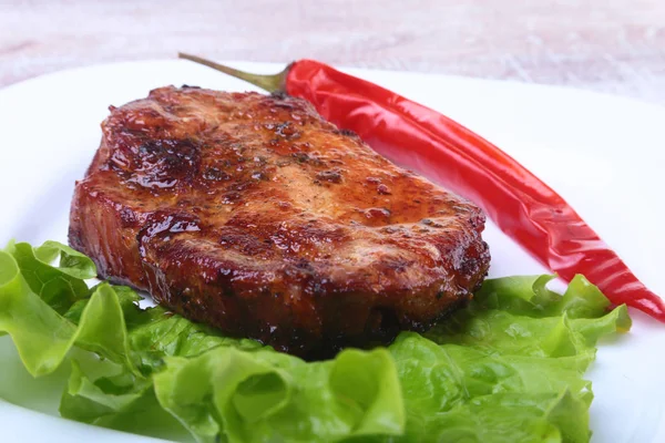 Biefstuk gegrild vlees en chili peper met tomaat, sla bladeren op een witte plaat. — Stockfoto