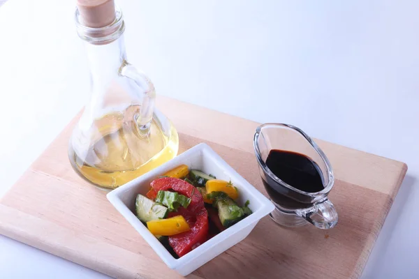 Sałatką ze świeżych warzyw z pomidora, ogórka, papryki, liść sałaty w misce biały, oliwy z oliwek i sosem balsamicznym w butelce. Selektywny fokus. — Zdjęcie stockowe