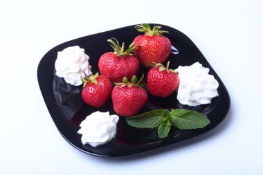 Krem şanti ve nane ile taze çilek siyah bir plaka üzerinde bırakır. Seçici odak.