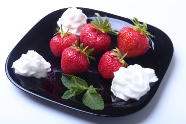 Krem şanti ve nane ile taze çilek siyah bir plaka üzerinde bırakır. Seçici odak.