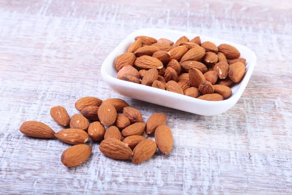 ahşap arka plan üzerinde beyaz kase fındık badem. Seçici odak.