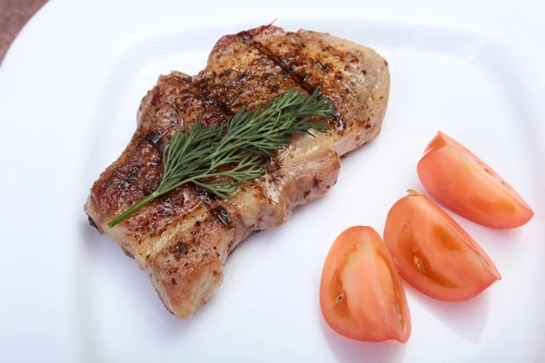Chuleta de cerdo a la parrilla con verduras en plato sobre tabla de madera — Foto de Stock