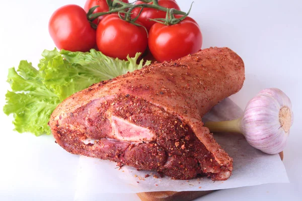 Çiğ domuz knuckle ve sebze, sarımsak, domates baharat ve marul yaprakları bir kesme tahtası üzerinde. Seçici odak. Hazır yemek pişirmek için.
