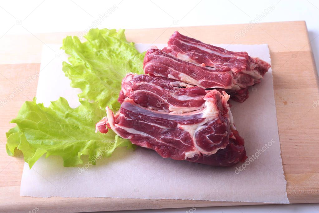 Raw beef edges and lettuce leaf on wooden desk isolated on white background from above and copy space. ready for cooking