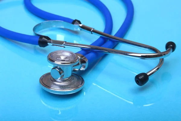 Medizinisches Stethoskop und rotes Herz auf blauem Spiegelhintergrund. Selektiver Fokus. — Stockfoto