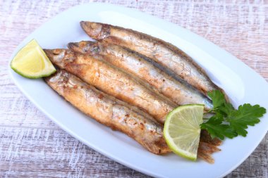 Küçük balık capelin ve beyaz tabakta dilimlenmiş limon kızartma derin. Bira için iyi snack.