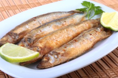 Küçük balık capelin ve beyaz tabakta dilimlenmiş limon kızartma derin. Bira için iyi snack.