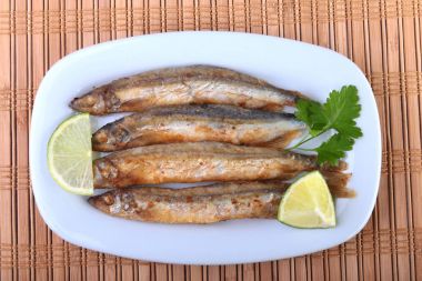 Küçük balık capelin ve beyaz tabakta dilimlenmiş limon kızartma derin. Bira için iyi snack.