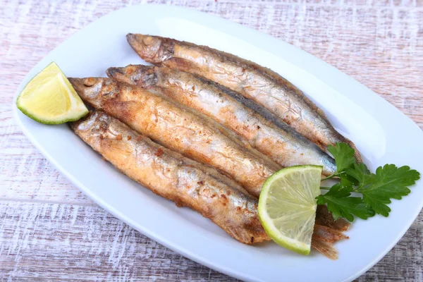 Küçük balık capelin ve beyaz tabakta dilimlenmiş limon kızartma derin. Bira için iyi snack.