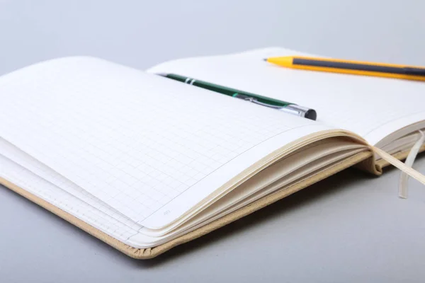 空白のページのノートブックを開くと白いテーブルの上にペン. — ストック写真