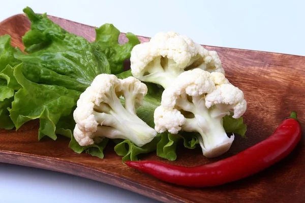 Свежая цветная капуста и зеленые листья салата на деревянной доске. вегетарианская еда. Готовы к приготовлению . — стоковое фото