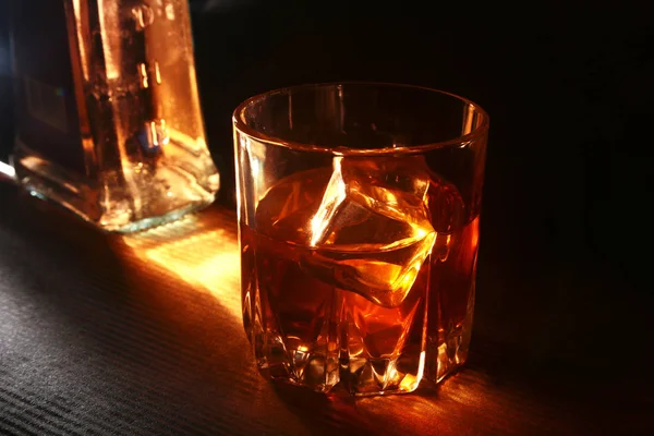 Bouteille et verre de whisky ou de bourbon avec glace sur table en pierre noire . — Photo