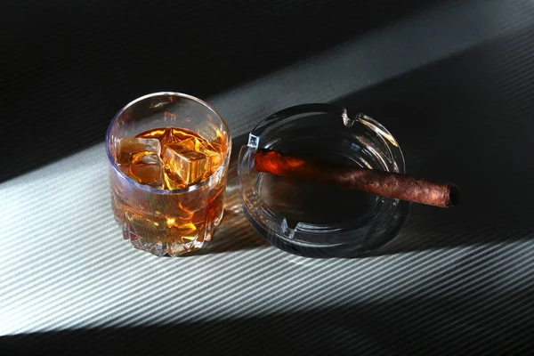 Glass of whiskey or bourbon with ice and cigar on black stone table. Selective focus. — Stock Photo, Image