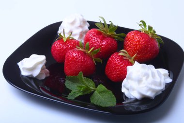 Krem şanti ve nane ile taze çilek siyah bir plaka üzerinde bırakır. Seçici odak.