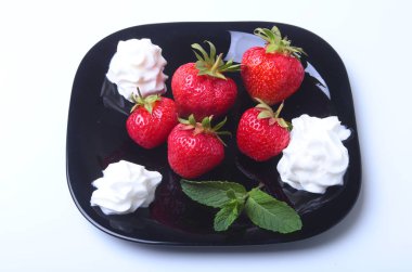 Krem şanti ve nane ile taze çilek siyah bir plaka üzerinde bırakır. Seçici odak.