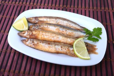 Küçük balık capelin ve beyaz tabakta dilimlenmiş limon kızartma derin. Bira için iyi snack.