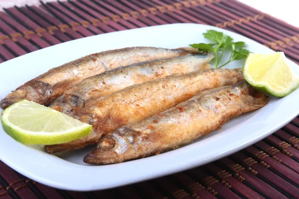 Küçük balık capelin ve beyaz tabakta dilimlenmiş limon kızartma derin. Bira için iyi snack.