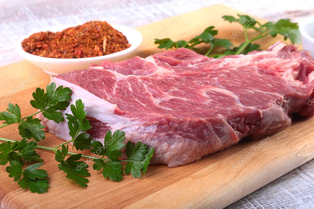 Raw beef steak with spices Leaves of coriander on wooden cutting board. Ready for cooking.